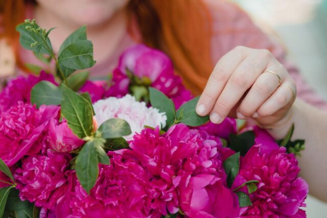 Bride and her florist reviewing fresh bunches of peonies, ranunculus, and eucalyptus spread across a wide wooden...