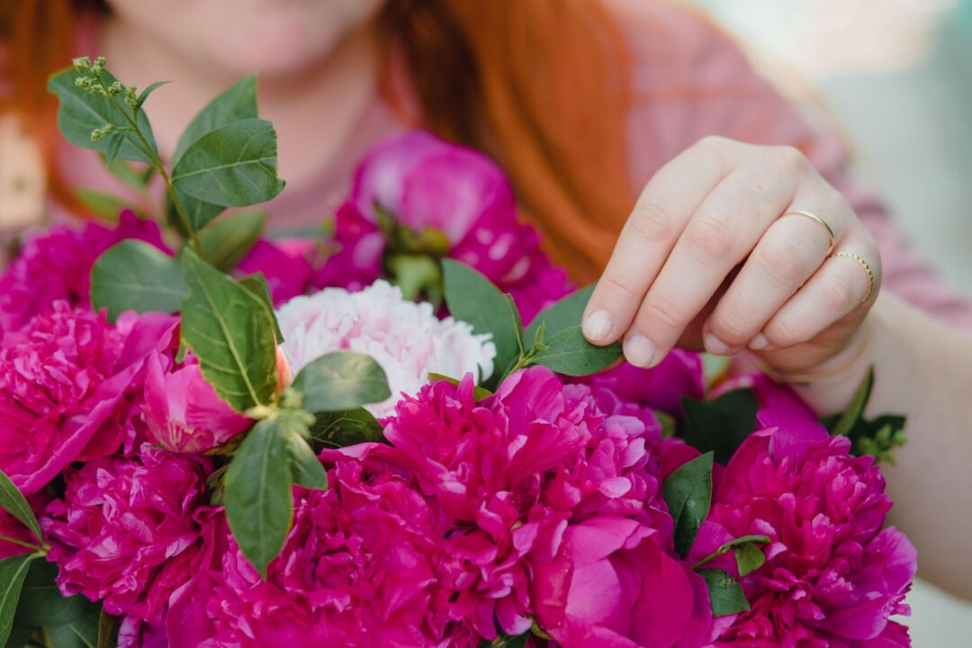 Bride and her florist reviewing fresh bunches of peonies, ranunculus, and eucalyptus spread across a wide wooden...