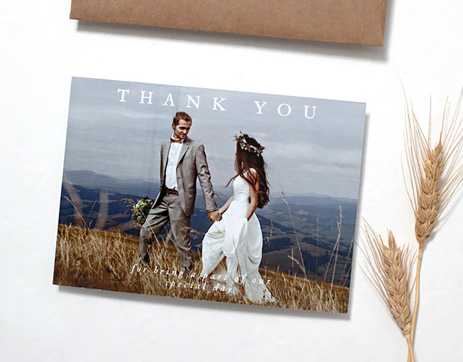 Paperlust Luna wedding thank you card, a landscape photo card with thank you wording over a couple walking through a mountain field, shown with a kraft envelope