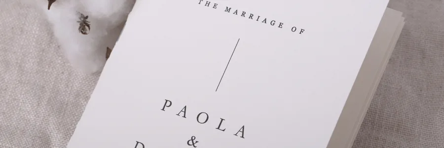 Paperlust A5 wedding program booklet cover reading The Marriage Of Paola and Daniel, styled with cotton stems