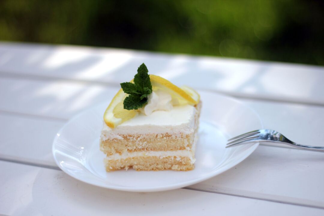 Plated slice of white buttercream wedding cake with a fresh edible flower garnish on a white porcelain plate, styled on a...
