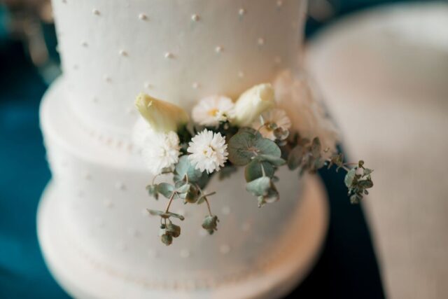 Elegant two-tier white buttercream wedding cake with fresh garden roses on a linen-draped dessert table next to a...