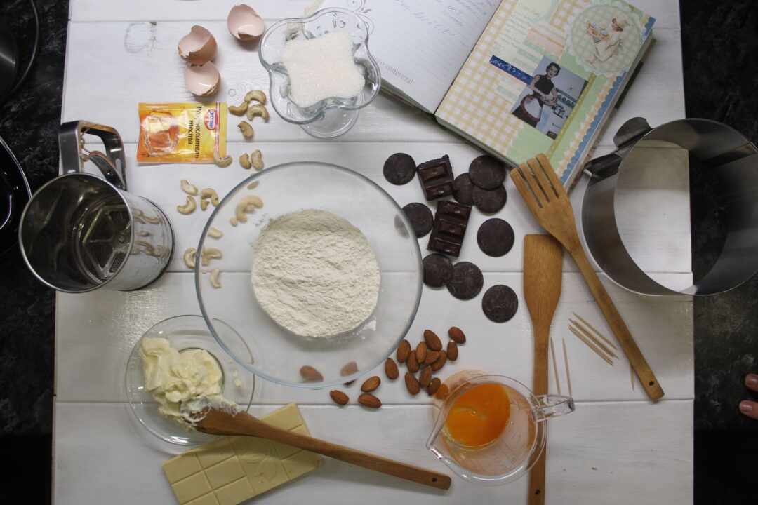Styled flat lay of artisan cake ingredients including a small bowl of pistachio nuts, dried lavender sprigs, fresh citrus...
