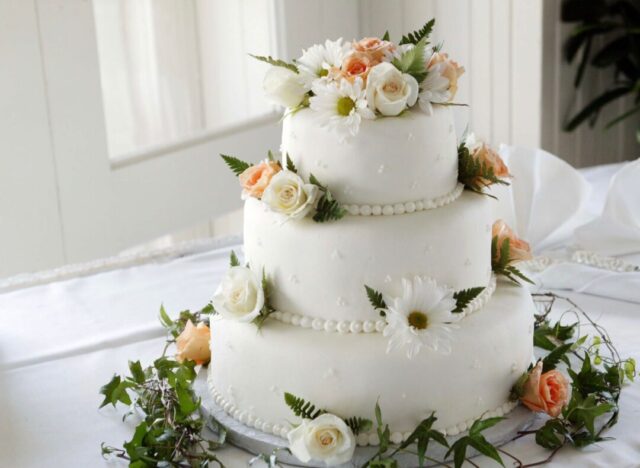 Three-tiered wedding cake with pistachio-green buttercream rosettes, fresh flowers, and a dusting of dried petals on a...