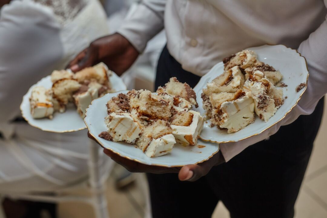 Wedding catering team plating individual slices of rectangular sheet cake onto white dessert plates in a professional...