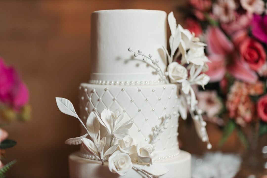 Three-tier white wedding cake with delicate hand-painted watercolor florals in blush and sage green on a marble cake...