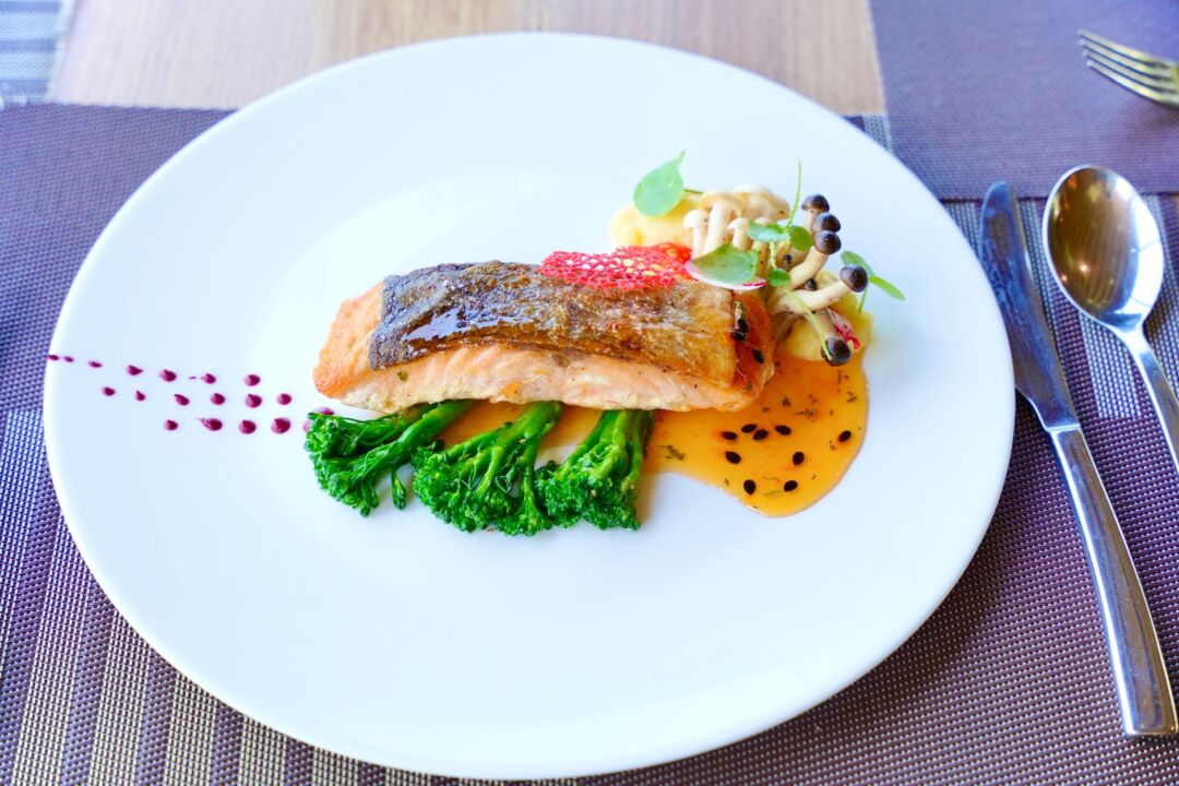 Close-up of an elegantly plated wedding dinner with a seared salmon entree, microgreens, and a gold-rimmed charger plate...