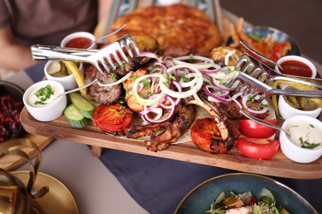 Wedding family-style dinner in progress, large ceramic platters of roasted vegetables and carved meats arranged along a...