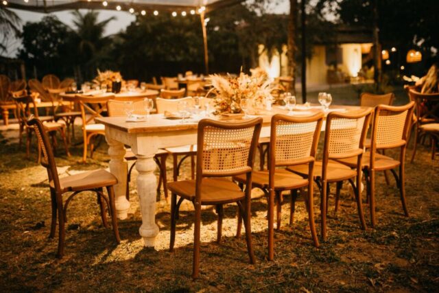 Elegantly set outdoor wedding reception under a clear-span tent, long family-style dining tables draped in white linen...
