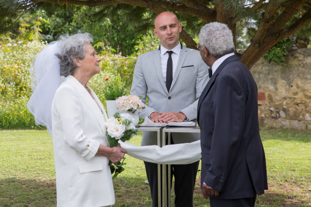 Close-up of an officiant holding small script cards with a white garden ceremony backdrop, fresh flowers visible at the...