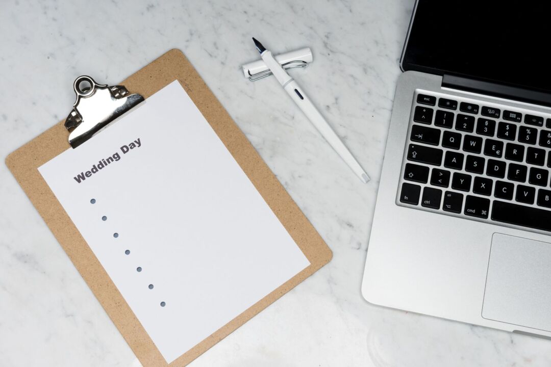 Organized planning desk with an open laptop, a printed checklist, a calendar, and a cup of coffee in bright natural...