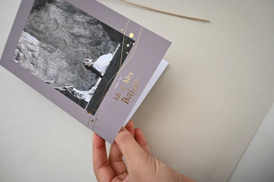 Paperlust Galaxies folded wedding thank you card in mauve with copper foil celestial lines and stars around a black and white couple photo, held in hand