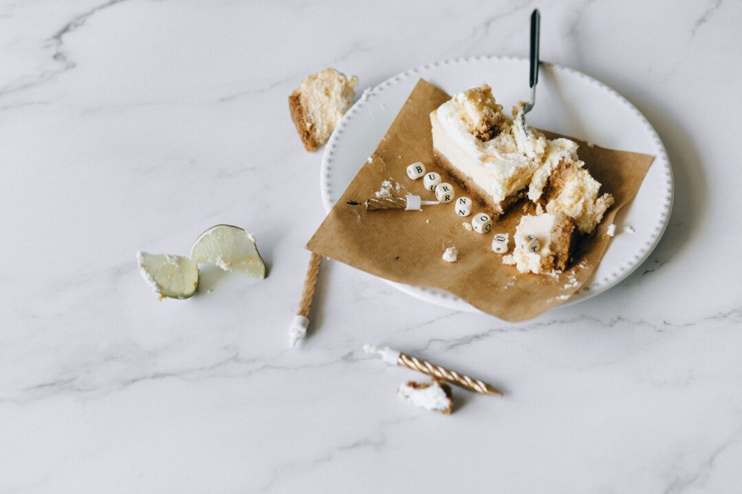 Close-up of four small white cake slices on a marble tasting board, each with a small handwritten label card describing...