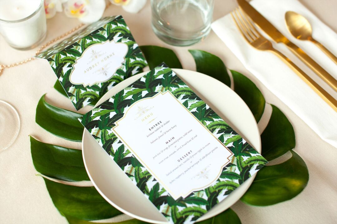 Beverly Hills Hotel wedding menu and matching folded place card in a green palm print with gold, set on a plate with monstera leaves and gold cutlery, Paperlust