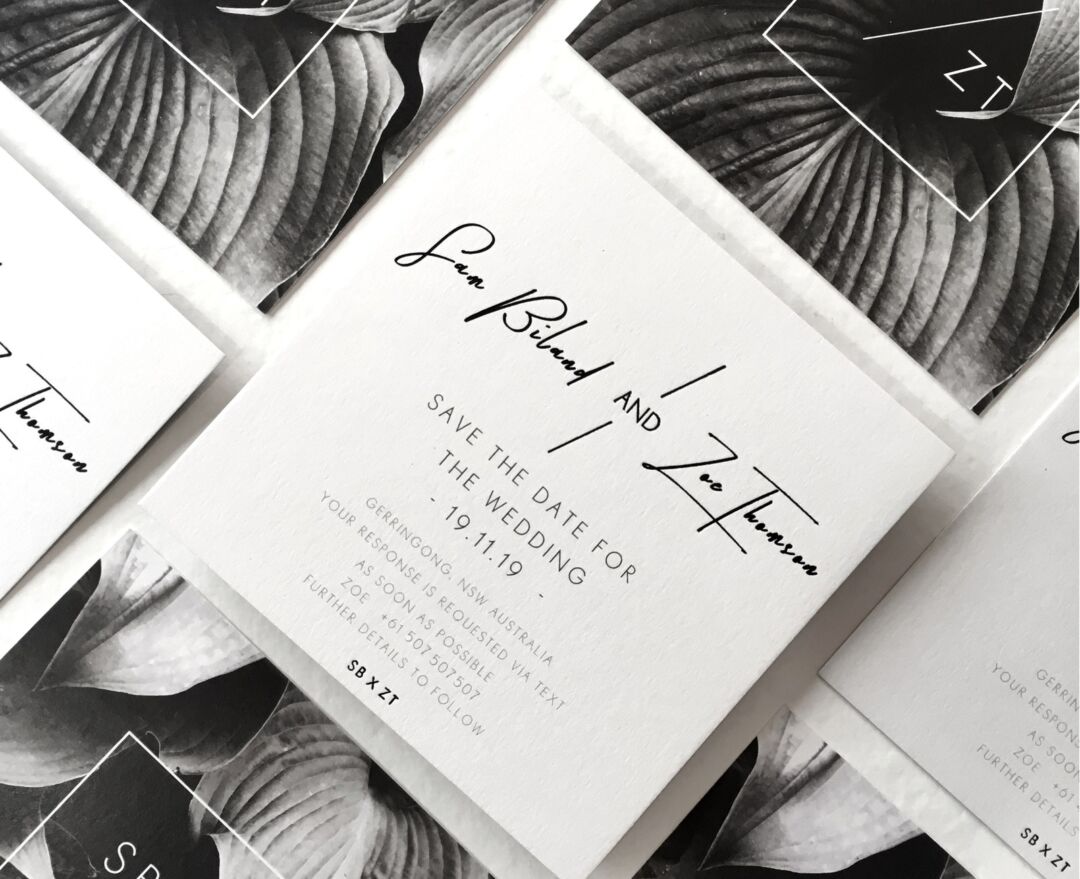 Modern Mode save the date cards in black hand lettering on white card, layered over a monochrome botanical backing print, Paperlust