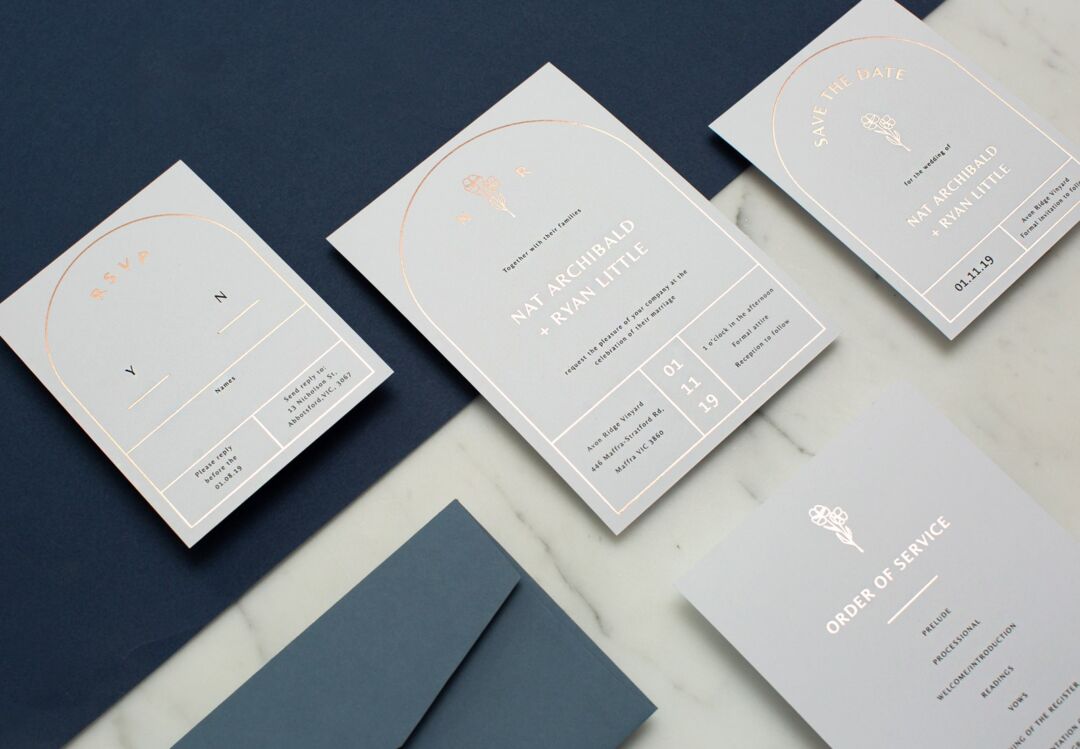 Rose Foil Arch wedding suite in copper foil on grey card, invitation with RSVP, save the date and order of service laid out on navy and marble, Paperlust