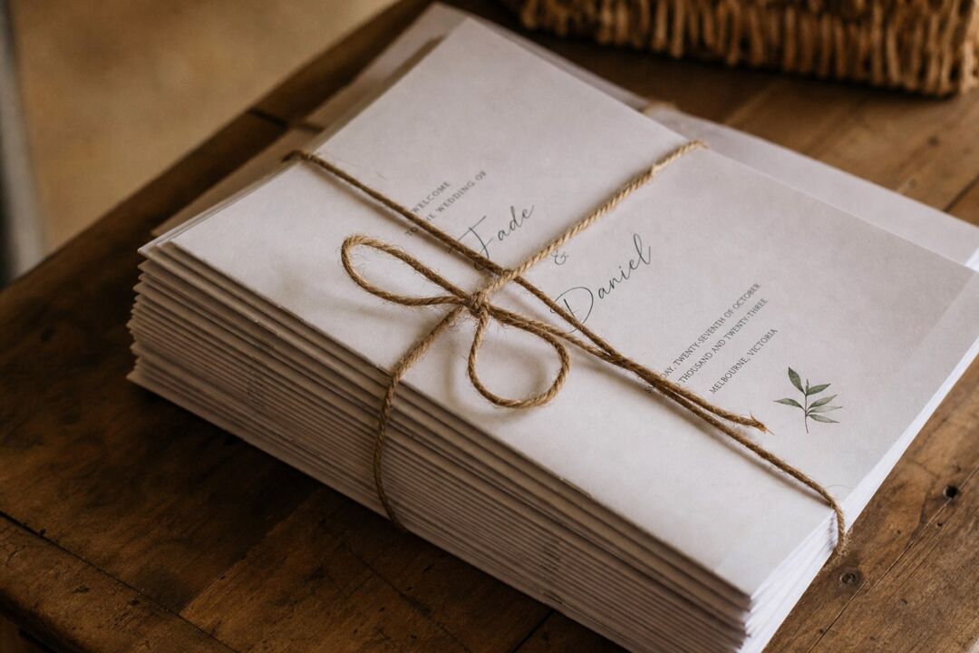 Stack of wedding ceremony program booklets tied with rustic twine on a wooden surface, partial text visible.