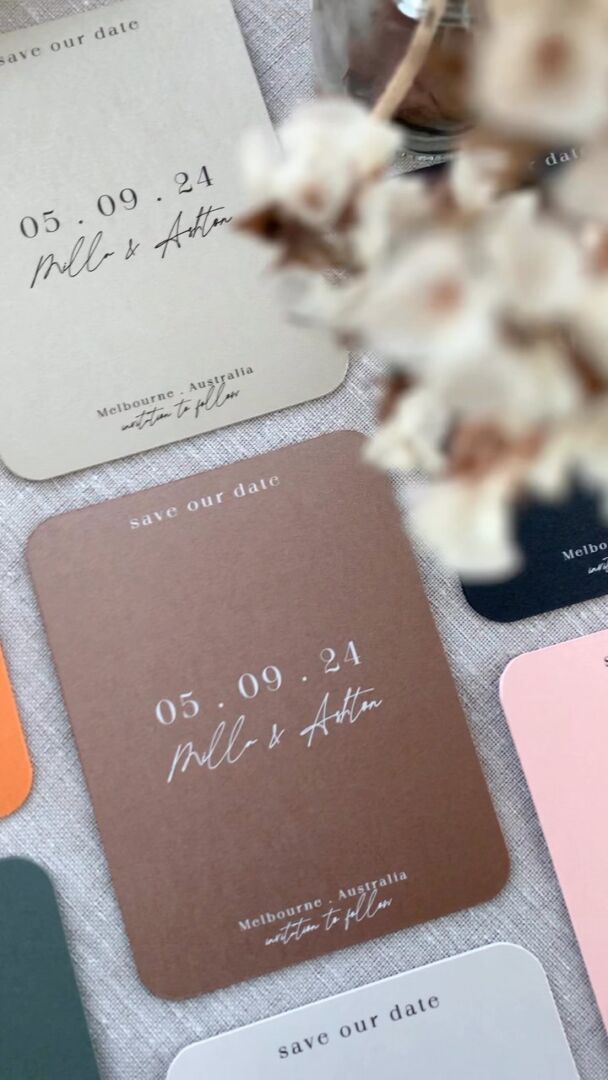Metallic save-the-date cards in multiple colors with dried flower accents.