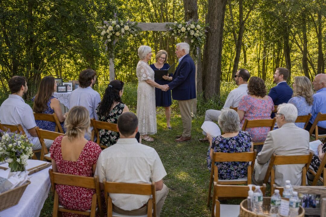 A small group of twelve to fifteen family members and friends seated in wooden folding chairs at an outdoor ceremony.