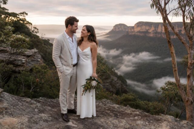 A couple standing at the edge of a sandstone lookout in the Blue Mountains.