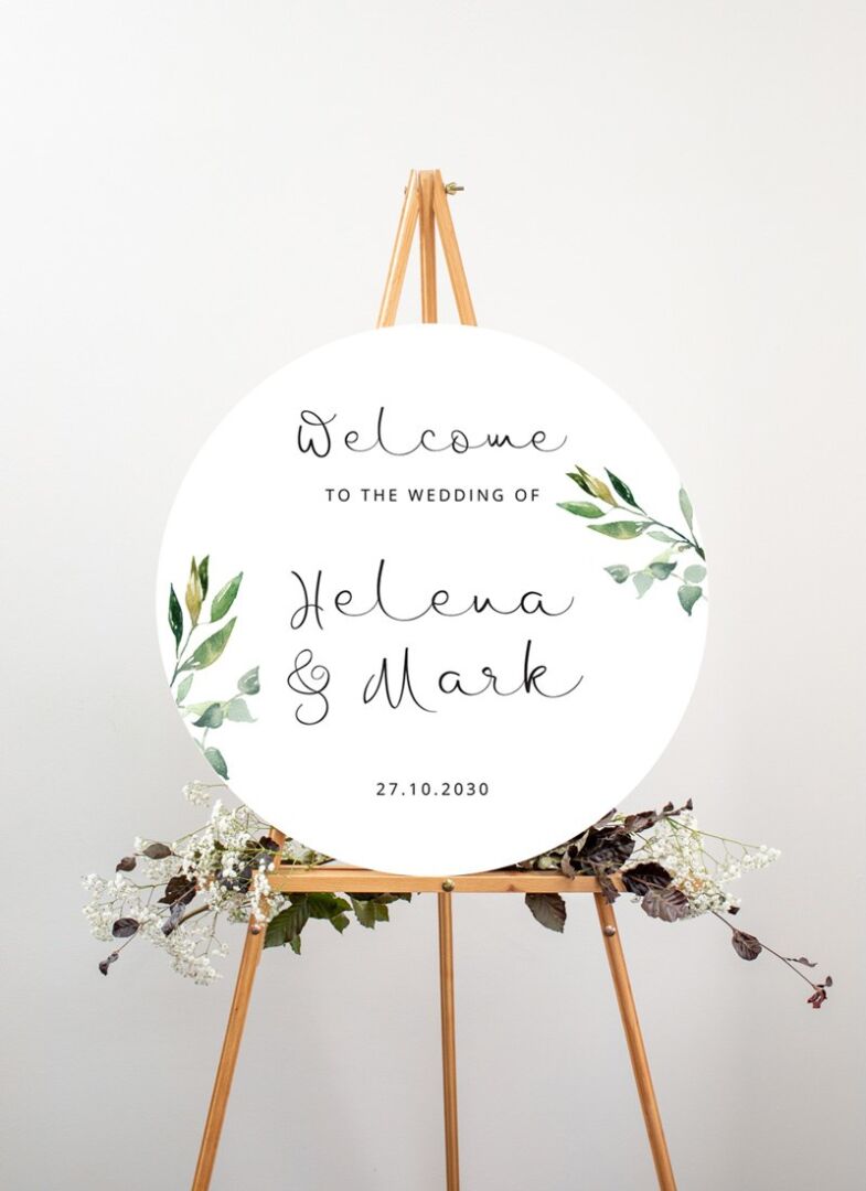 A Paperlust circular welcome sign on a timber easel dressed with greenery.