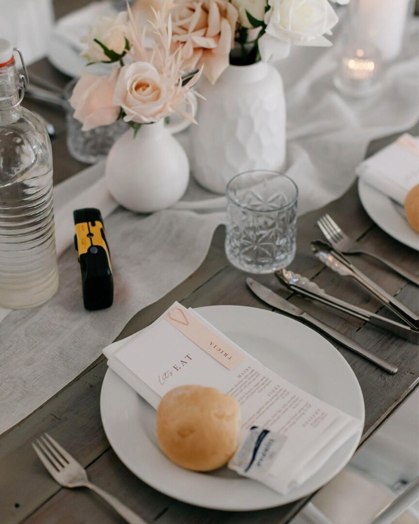 A Paperlust printed wedding menu on a plate at a styled reception place setting, with linen, glassware and blush florals.