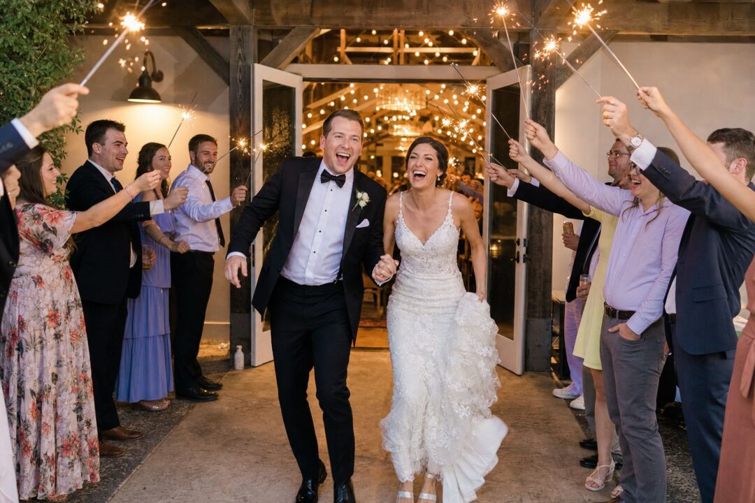 A bride and groom making their grand entrance through a corridor of guests holding sparklers.
