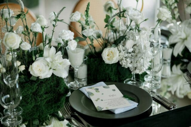 An elegant table setting features white flowers and greenery with a place card reading 'Gifts' on a dark plate.