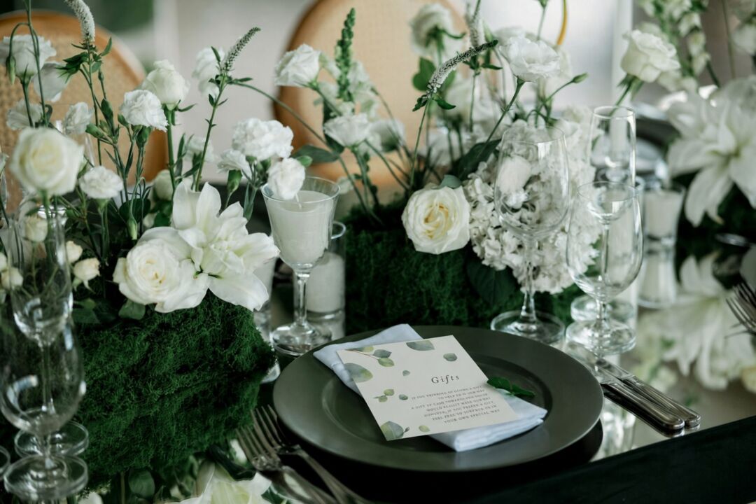 An elegant table setting features white flowers and greenery with a place card reading 'Gifts' on a dark plate.