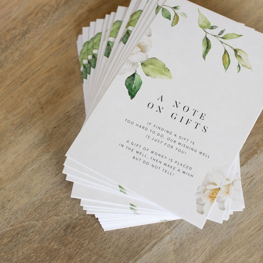 A stack of white cards with green leaf watercolor designs and 'A Note on Gifts' text lies on a wooden surface.