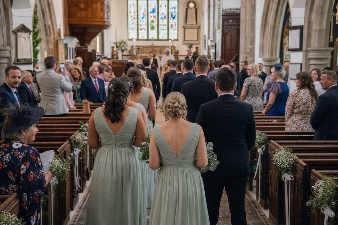 Wedding party lined up in a church processional, bridesmaids in matching gowns and groomsmen in dark suits.