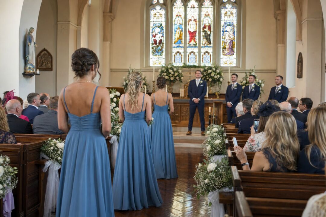 Processional from the rear of a flower-lined aisle in a bright chapel.