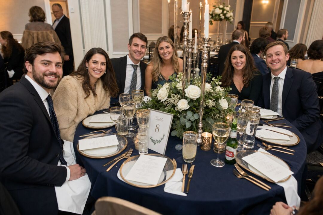 A winter wedding reception round table with navy tablecloth, tall silver candlestick centerpieces, white and ivory rose floral arrangements.