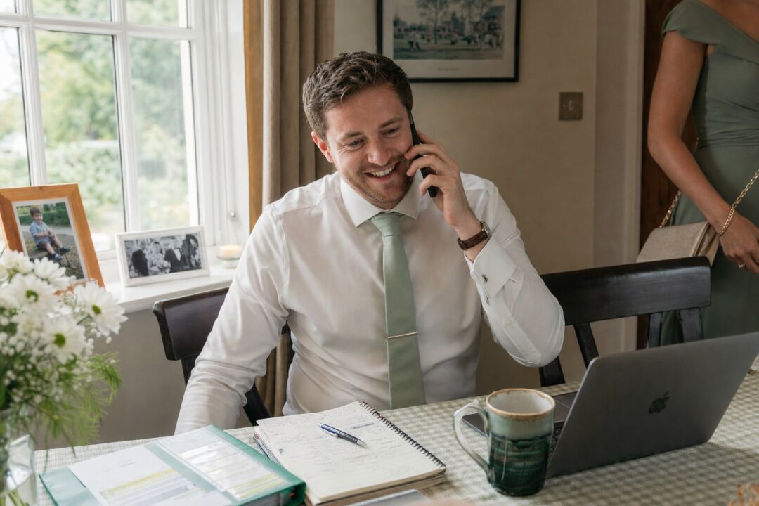 A person holding a phone to their ear and smiling, seated near a window with afternoon light, visibly in a happy private conversation.