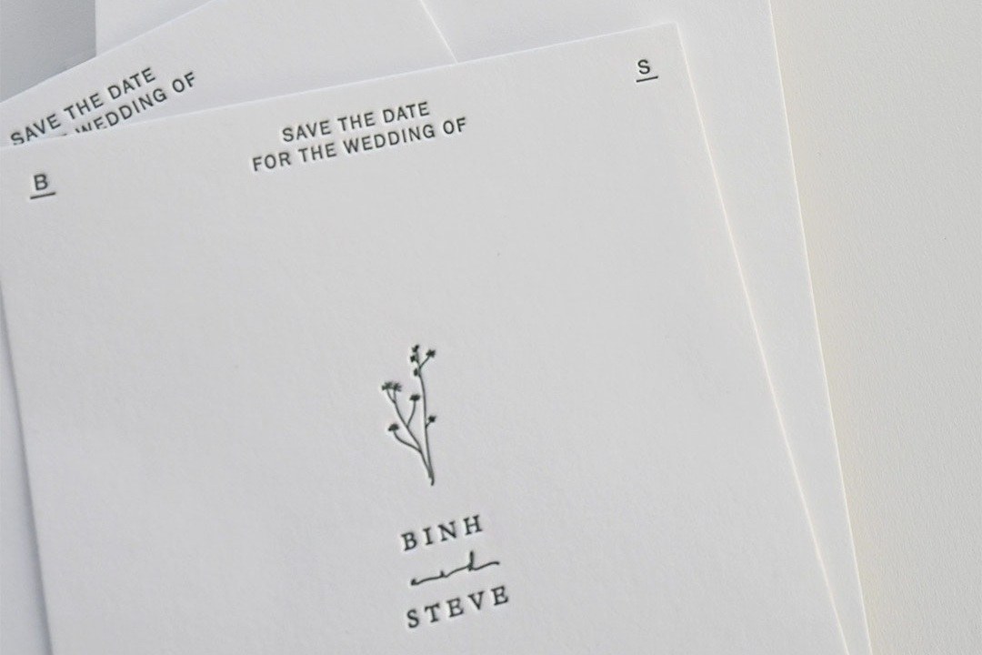 Several cream-coloured save the date cards fanned out, each with a minimalist botanical illustration above the couple's names.