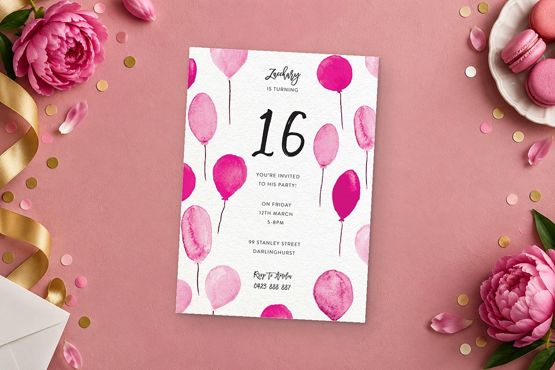 Paperlust Birthday Balloons invitation with pink watercolor balloons sits on dusty rose beside pink peonies and gold ribbon.