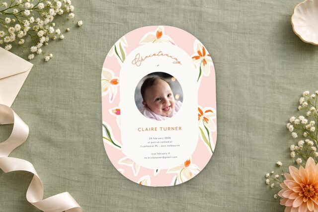 Paperlust Bright Blush Flower christening invitation rests on sage green linen beside a peach dahlia and a cream envelope.