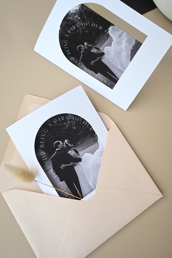 Two thank you cards with arched black and white photos lie on beige, the lower one in a blush envelope with bunny tail grass.