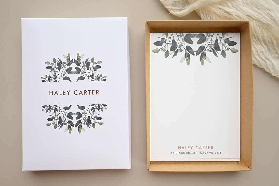 Paperlust Garden Estate lid with green eucalyptus and Haley Carter in copper foil sits beside white notecards on a beige surface.