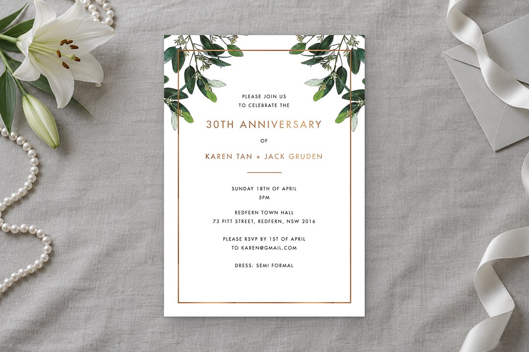 Paperlust Garden Estate portrait invitation with eucalyptus leaves and copper border rests on gray linen beside pearls.