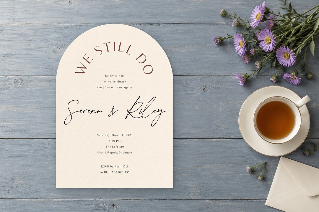 Paperlust Impressionist cream arch invitation rests on gray blue boards with a white teacup, purple asters, and an envelope.
