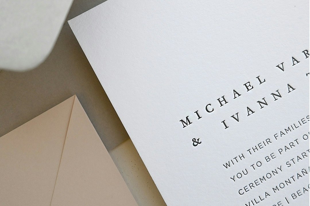 Paperlust Nouveau thick white cotton invitation corner shows black letterpress names Michael and Ivanna above blush envelopes.