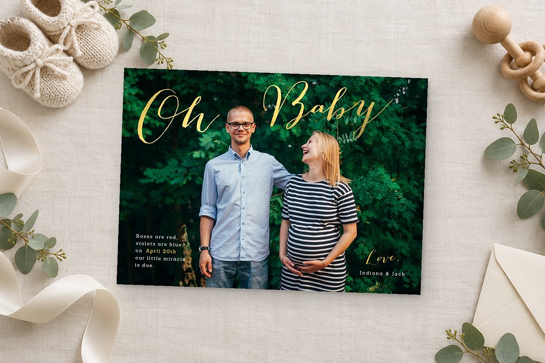 Paperlust Sneak Peek pregnancy announcement card rests on linen with knitted booties, eucalyptus and gold Oh Baby script.