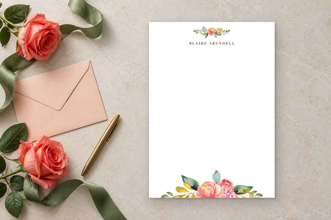 Paperlust Spring Bouquet notecard with watercolor coral pink flowers rests on pale stone beside rose stems and jade ribbon.