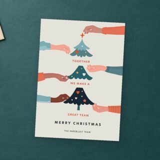 Paperlust Teamwork card on a deep teal desk is surrounded by a cream envelope, fir sprigs, coral and cream paper stars, and a brass pen.