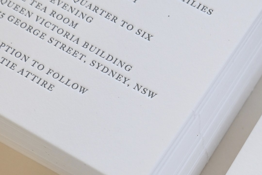 Stacked thick white cotton invitations show dark gray letterpress text reading quarter to six at Queen Victoria Building.